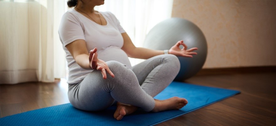 Pregnant woman practicing antenatal yoga in a seated meditation pose with an exercise ball in the background — BirthRight by Rainbow Hospitals