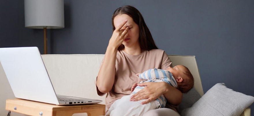 New mother holding her baby while feeling stressed and exhausted, showing signs of postpartum depression — BirthRight by Rainbow Hospitals.
